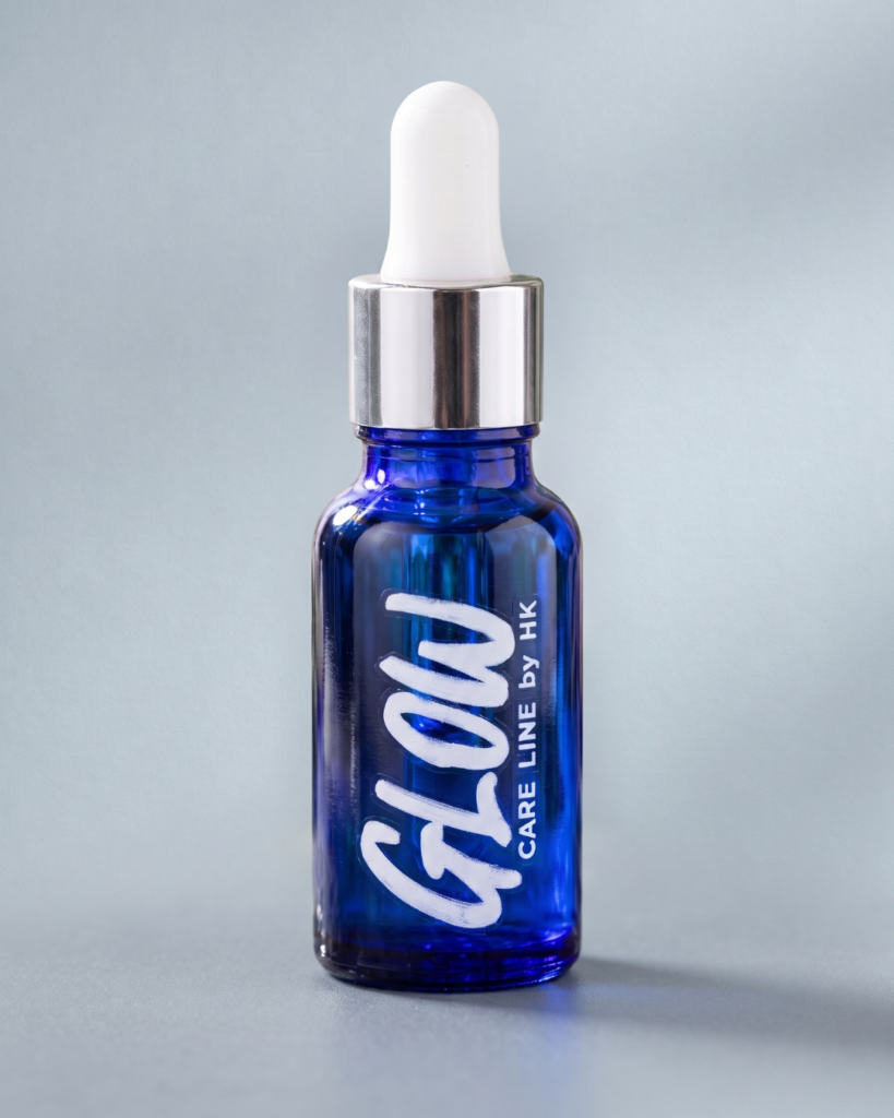 Aceite para barba Glow en frasco gotero de vidrio azul con gotas de agua sobre fondo claro